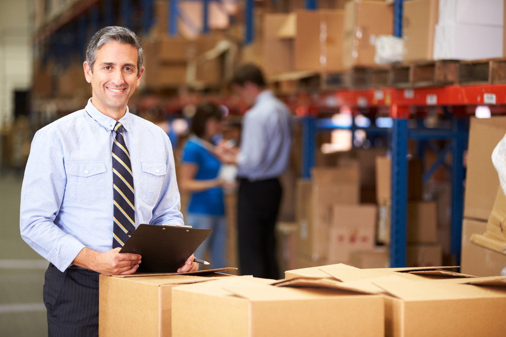 Man in a warehouse smiling by boxes ready to ship out.