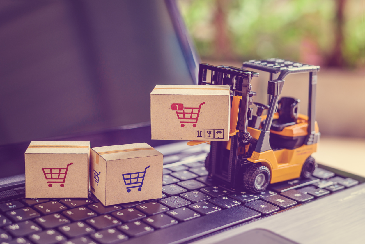 Logistics and supply chain management for online shopping concept : Fork-lift moves a box with a red shopping cart logo, 2 cartons on a laptop computer. The image depicting delivering goods or products in a store.